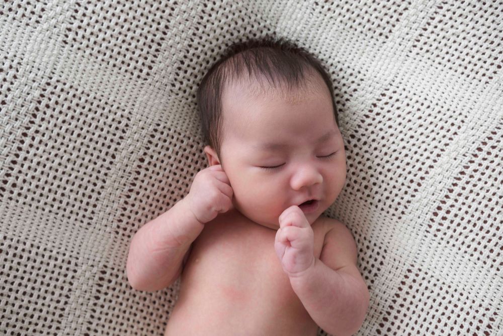 newborn baby boy on blanket during newborn photo session with Queens Photographer.