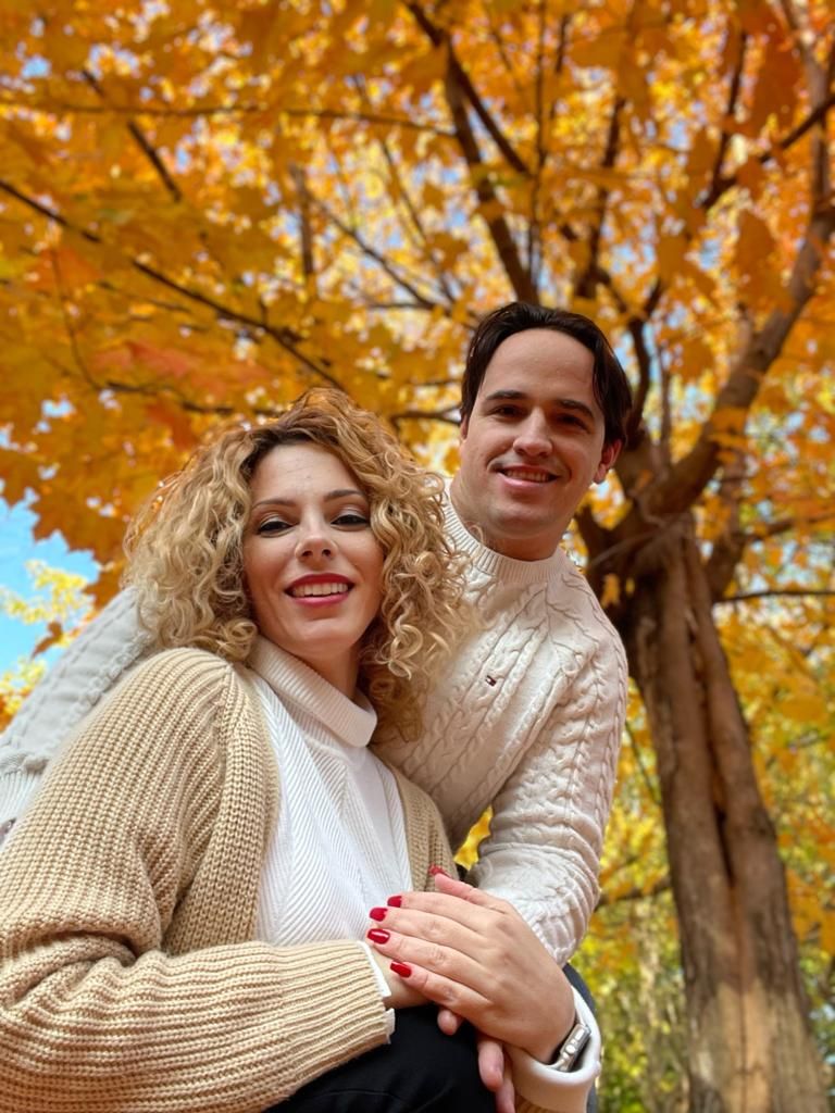 Couple in sweaters embracing under golden autumn maple tree foliage.