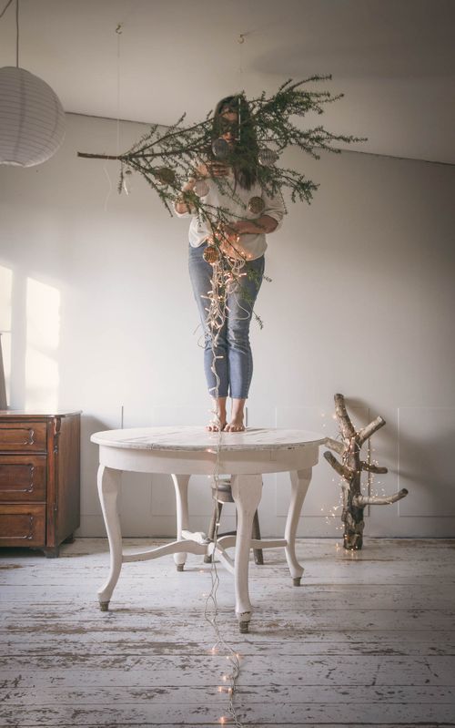 Person standing on white table holding large decorative branch with paper lantern in background.