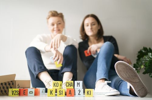Two people sitting with colorful letter blocks on floor in casual outfits.