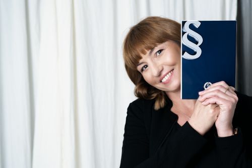 Person holding blue book against white curtain background with cheerful expression.