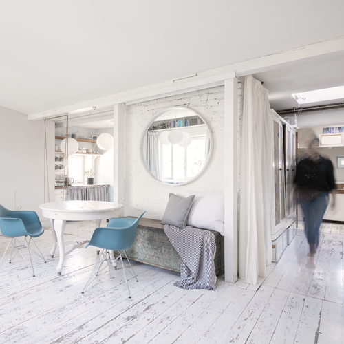 Modern white dining room with blue chairs and round mirror decor.