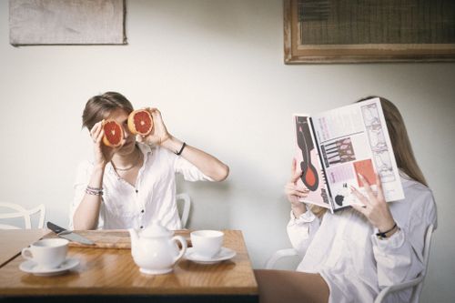 Two people enjoying coffee while playfully covering faces with newspaper and oranges.
