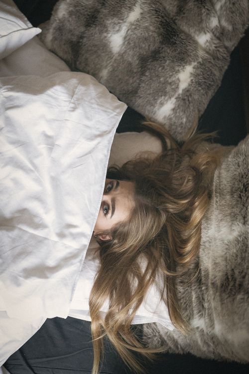 Relaxing on a cozy bed with gray fur throw and white bedding.