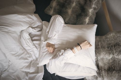 A cozy bed with white pillows and blankets on a gray fur throw.