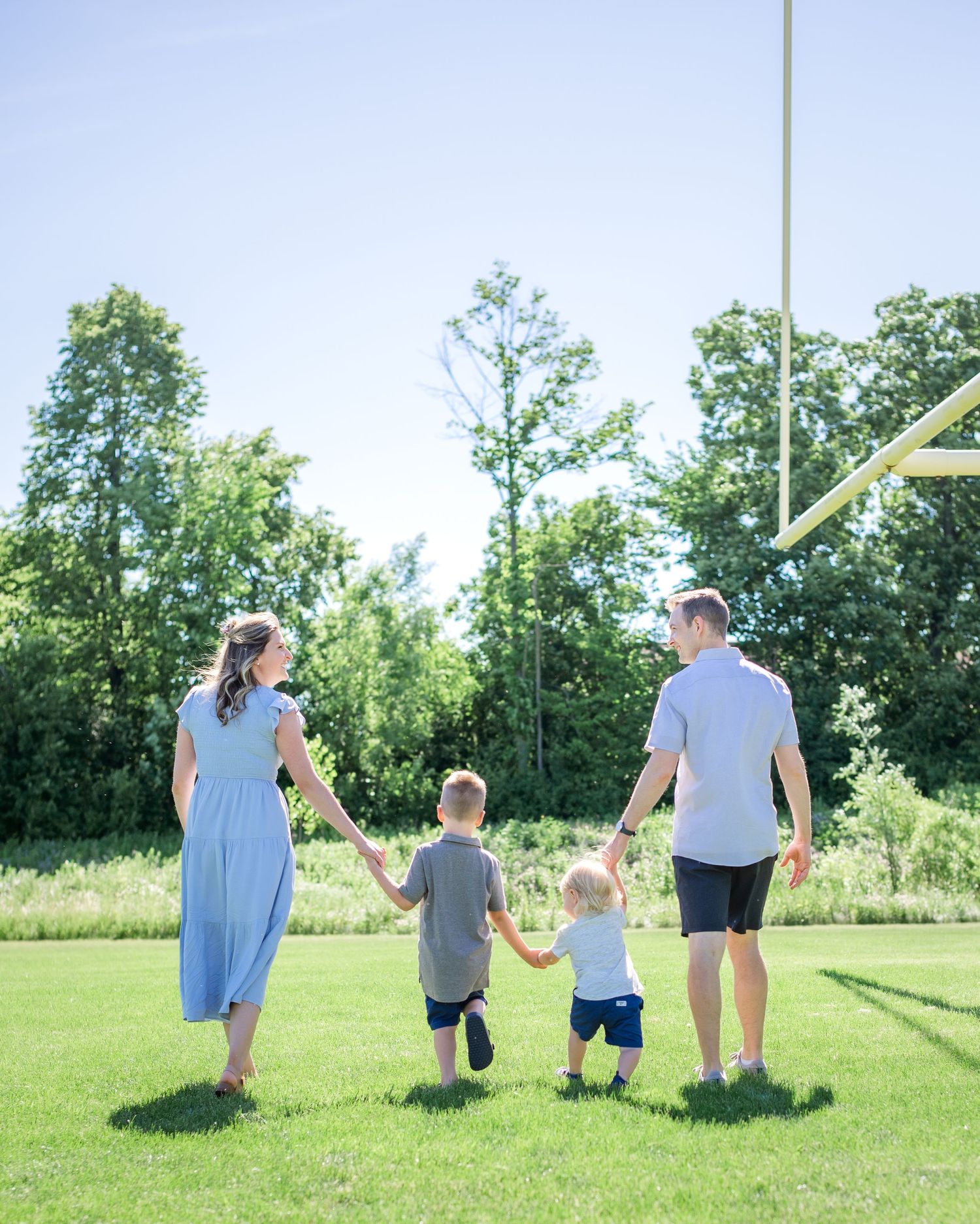 A family walks hand in hand through a grassy field on a bright summer day.