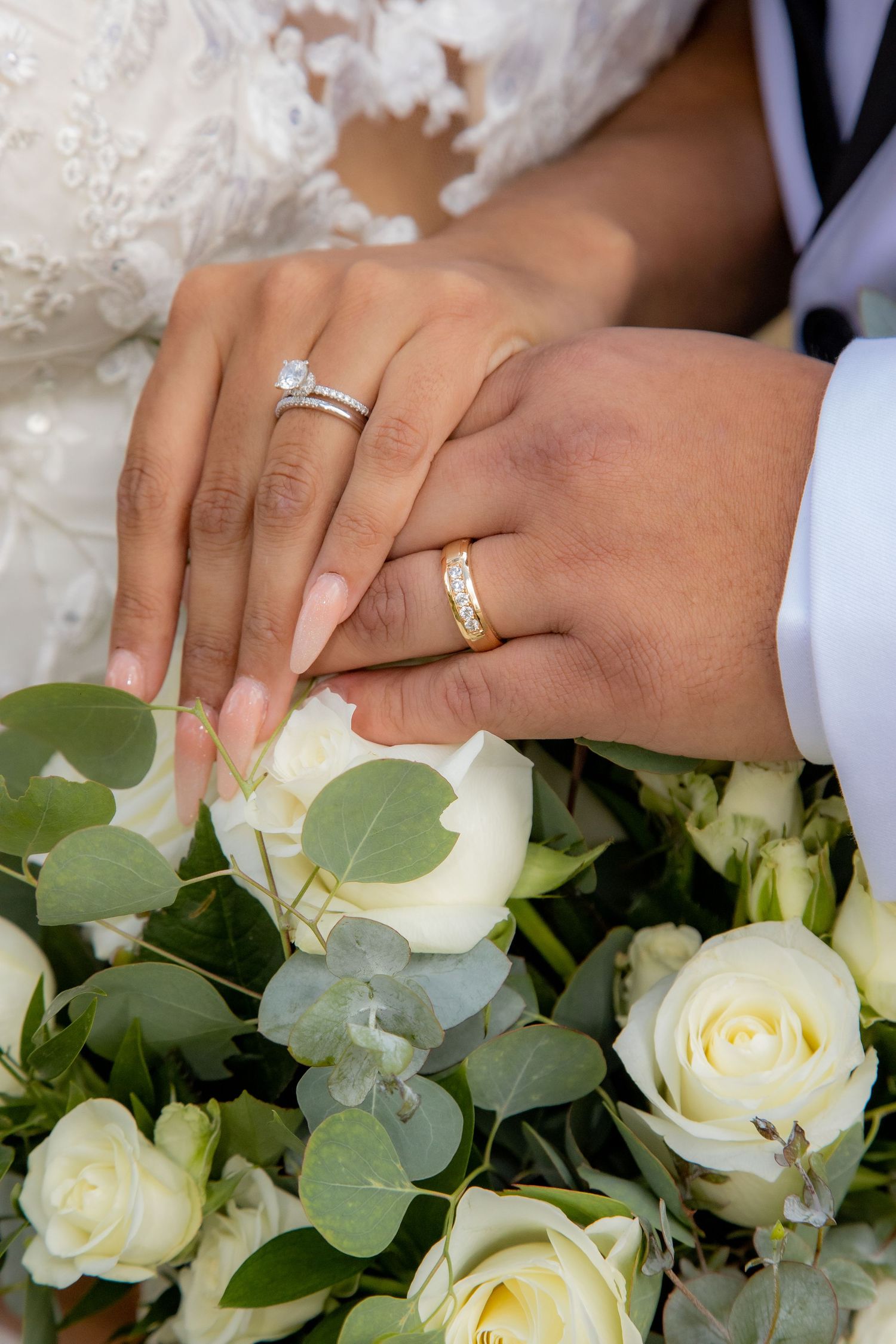 Newlyweds display wedding rings resting hands on a bouquet of white roses and eucalyptus.
