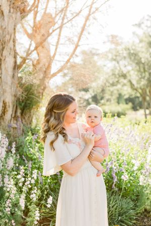 Ethereal garden portrait with wildflowers as woman holds baby in pink outfit.