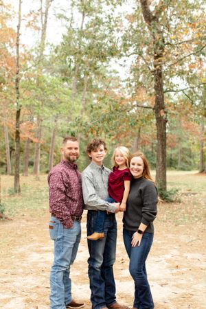 A family poses together on a dirt path surrounded by fall foliage in a wooded setting.