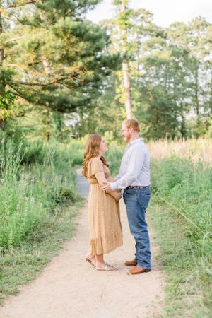 A romantic maternity photoshoot on a nature trail surrounded by tall grass and pine trees.