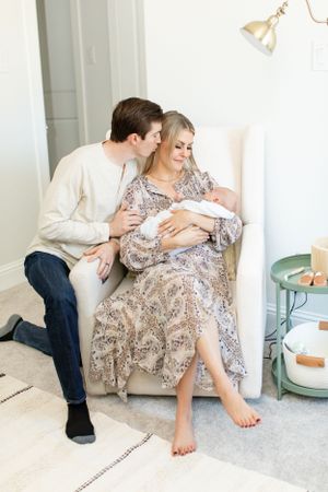 Parents share an intimate moment with their newborn on a plush chair.