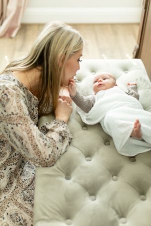 Mother in floral dress shares tender moment with baby on tufted ottoman.