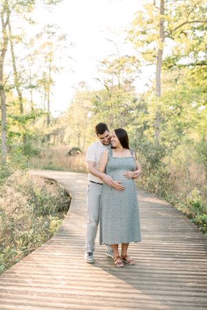 A couple embracing on a wooden boardwalk surrounded by lush greenery.