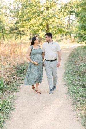 A couple walking together on a nature trail during golden hour as the sun filters through trees.