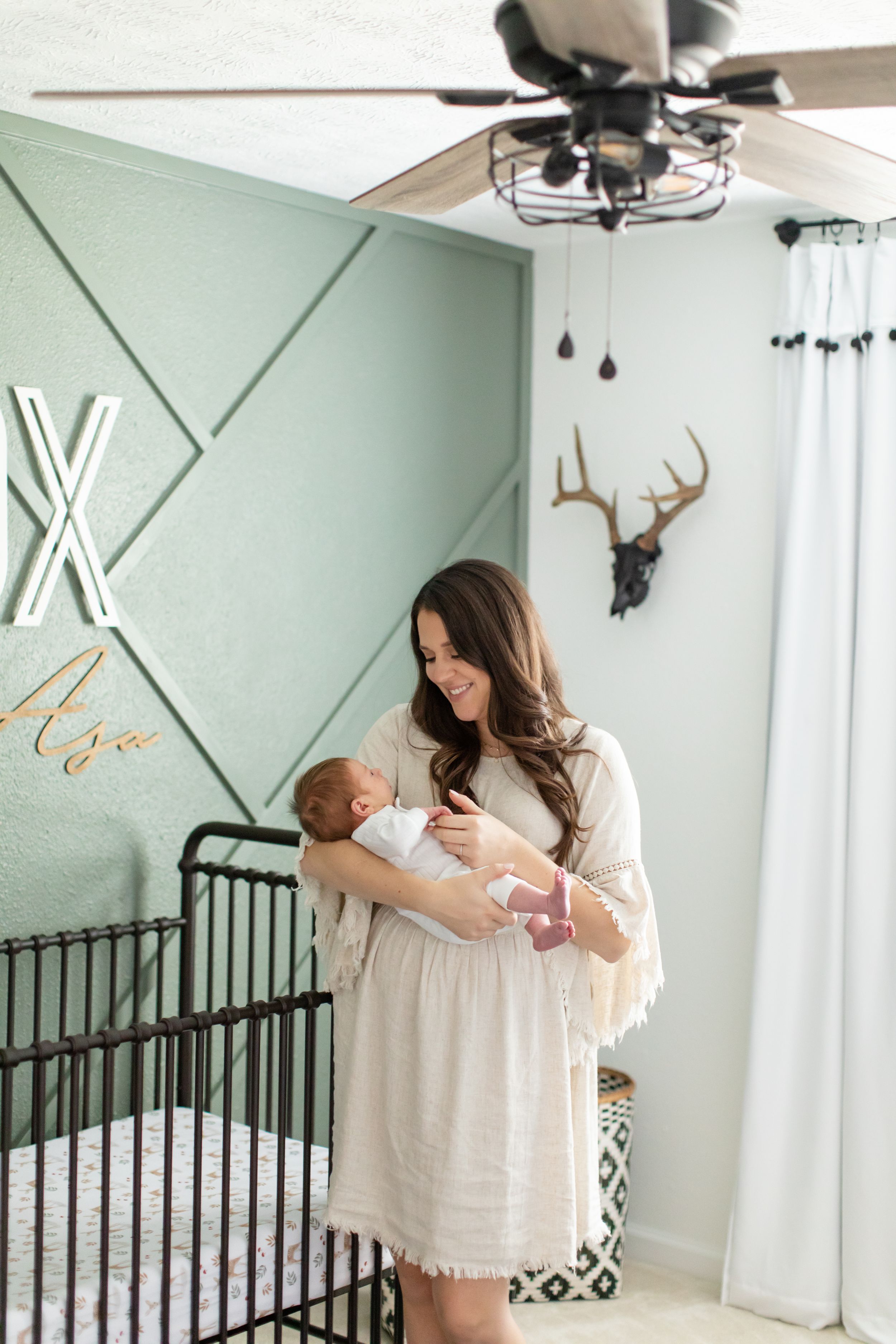 A tender moment in a modern nursery with sage green walls and geometric accents.