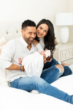 Couple in casual attire sharing tender moment with newborn on white bed.