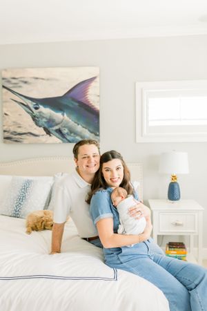 Family poses on bed with newborn baby and marlin artwork in background.