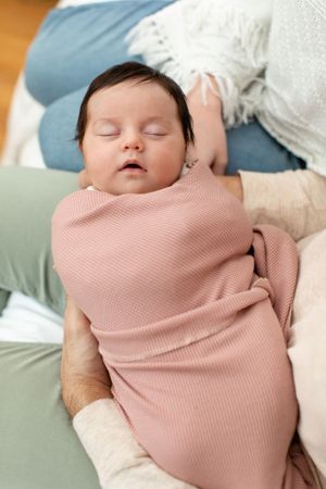 Baby sleeping peacefully while swaddled in pink knit fabric.