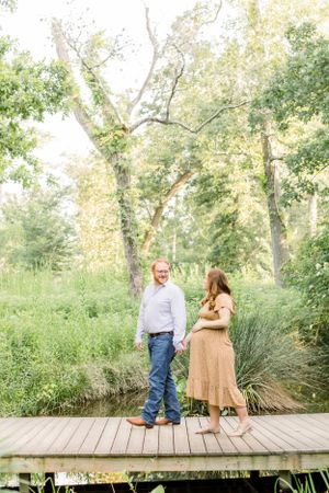 A couple shares a moment together on a wooden boardwalk surrounded by lush summer foliage.