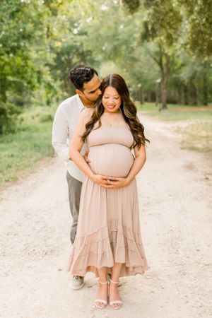 Intimate maternity portrait on woodland path with couple in neutral colored outfits.