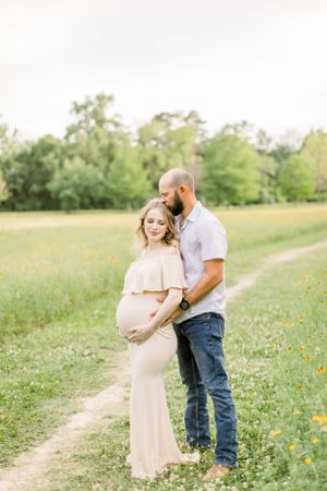 Maternity photoshoot on a serene dirt path surrounded by wildflowers and green grass.