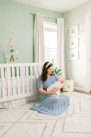 Nursery scene with mint green walls, white crib, and tender moment on patterned rug.