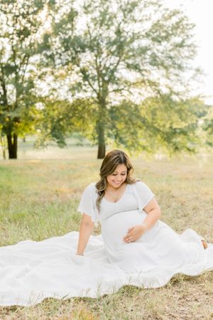 Woman in white dress sitting gracefully on blanket in sunlit field.
