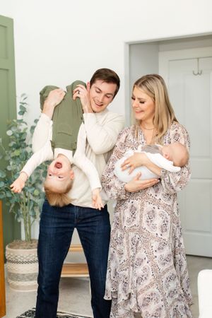Family having fun at home with one parent playfully holding a child upside down.
