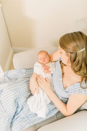 A tender moment between parent and newborn baby resting together on blue and white bedding.