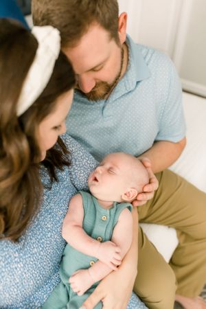 Tender family moment with a sleepy newborn baby wearing a teal romper.