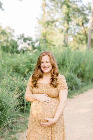 A maternity photoshoot featuring a floral yellow sundress in a natural outdoor setting with soft sunlight.
