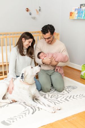 Family moment in nursery with white dog as parents hold newborn baby.