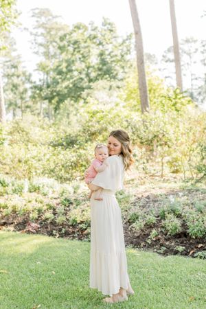 Sun-dappled garden scene with woman holding baby against natural landscaping.