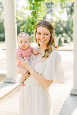 Mother and baby pose together on a bright white columned porch.