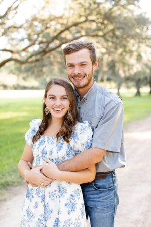 A happy couple embraces while posing for a portrait in a sunlit park setting.