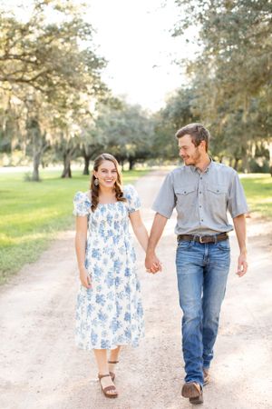 A couple walks hand in hand down a tree-lined dirt path during golden hour.