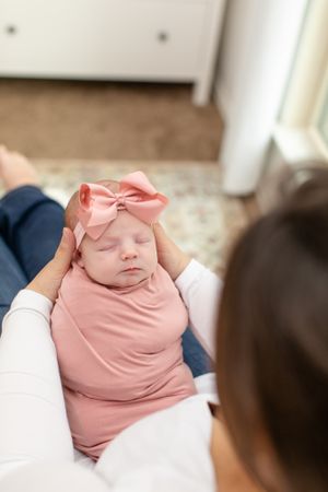 Sleeping newborn baby wearing pink outfit with matching bow headband.