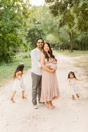 Family moment captured on dirt path with children playing in matching white dresses.