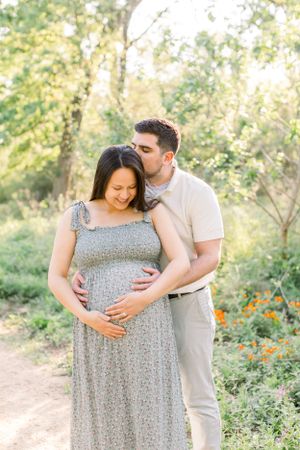 A tender maternity moment captured in a sun-dappled garden setting.