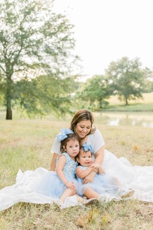 Tender family moment captured on a white blanket in a sun-dappled field.