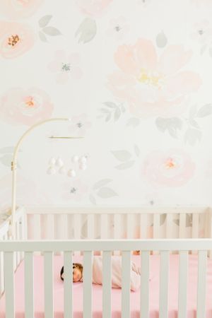 White crib against soft pink floral wallpaper in a minimalist nursery setting.