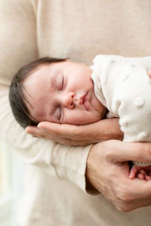 Close-up of sleeping newborn baby cradled in gentle hands.