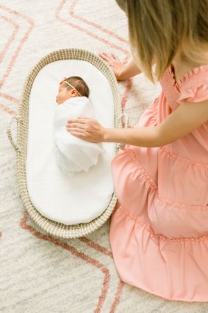 Baby sleeps peacefully in moses basket while being gently tended to.