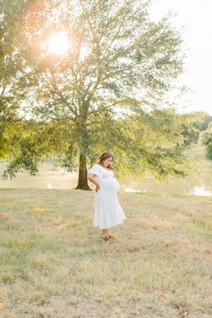 An ethereal maternity portrait captured at golden hour features a white-dressed figure in a peaceful outdoor setting.