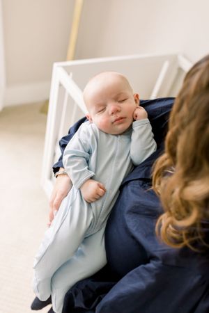 Sleeping baby in light blue sleeper rests peacefully on lap in nursery setting.