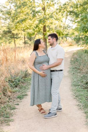 An expectant couple shares a loving moment on a sunlit nature trail.