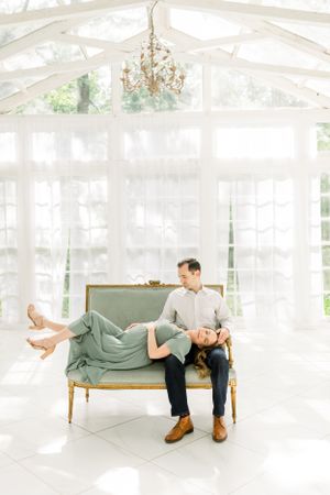A romantic maternity photo of a couple lounging on a vintage settee under a chandelier.