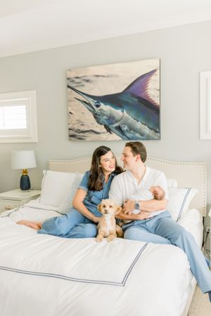 Family relaxes on bed with small dog and baby under marlin artwork.