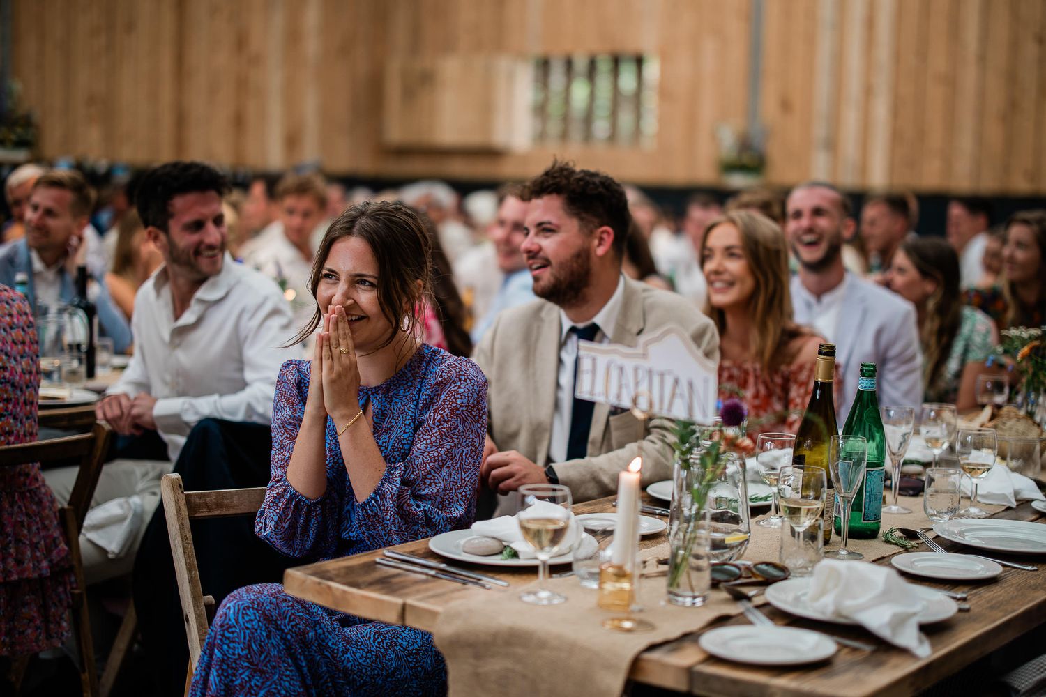 Wedding guests smile at a touching speech during a boho inspired wedding reception at The Grain Store.