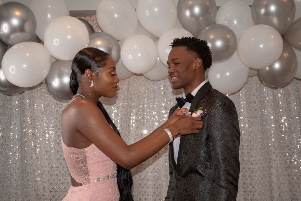 Formal couple celebrating at event with silver and white balloon backdrop.